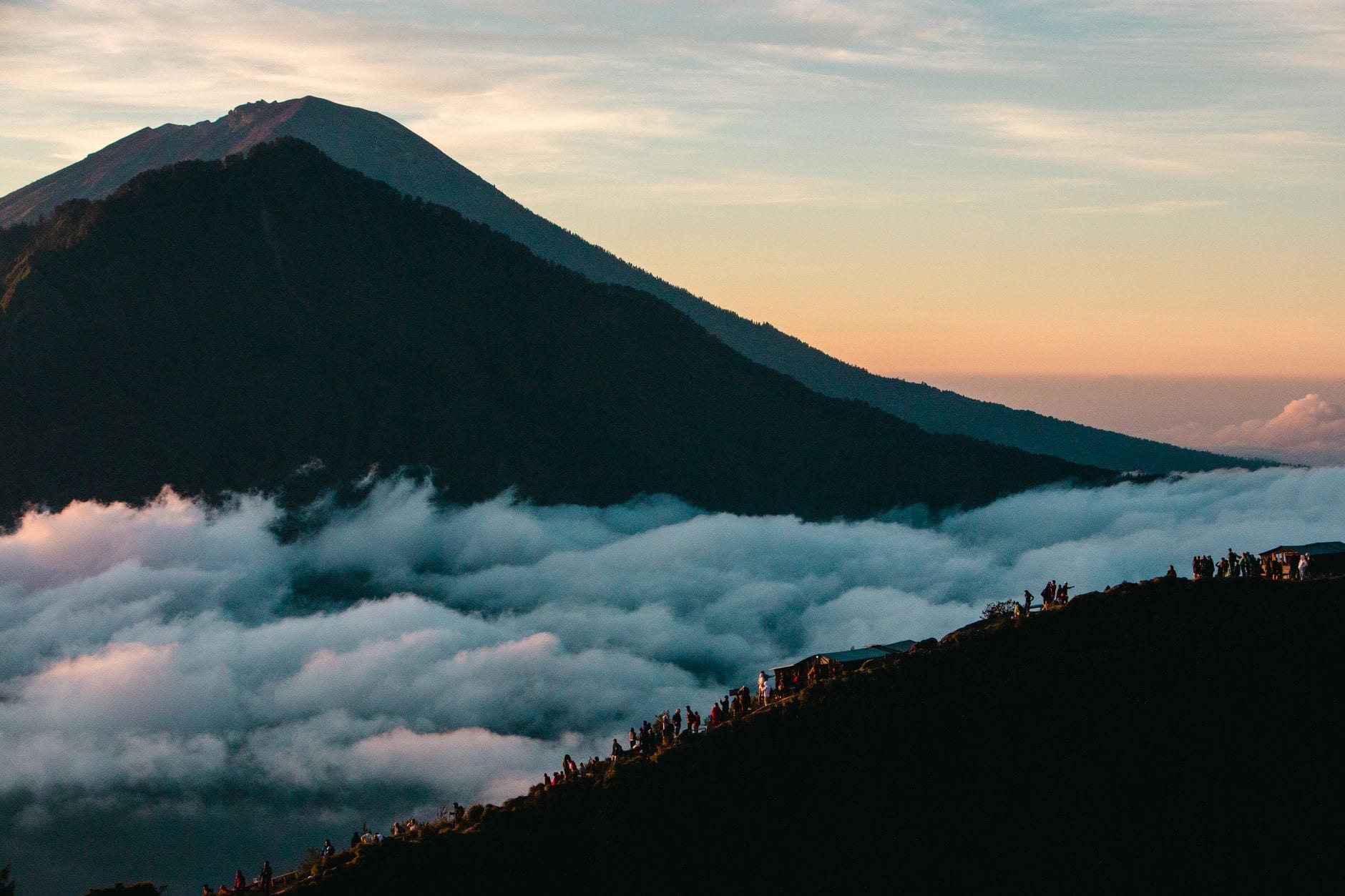 Hikers following a volcanic ridge above clouds at dawn