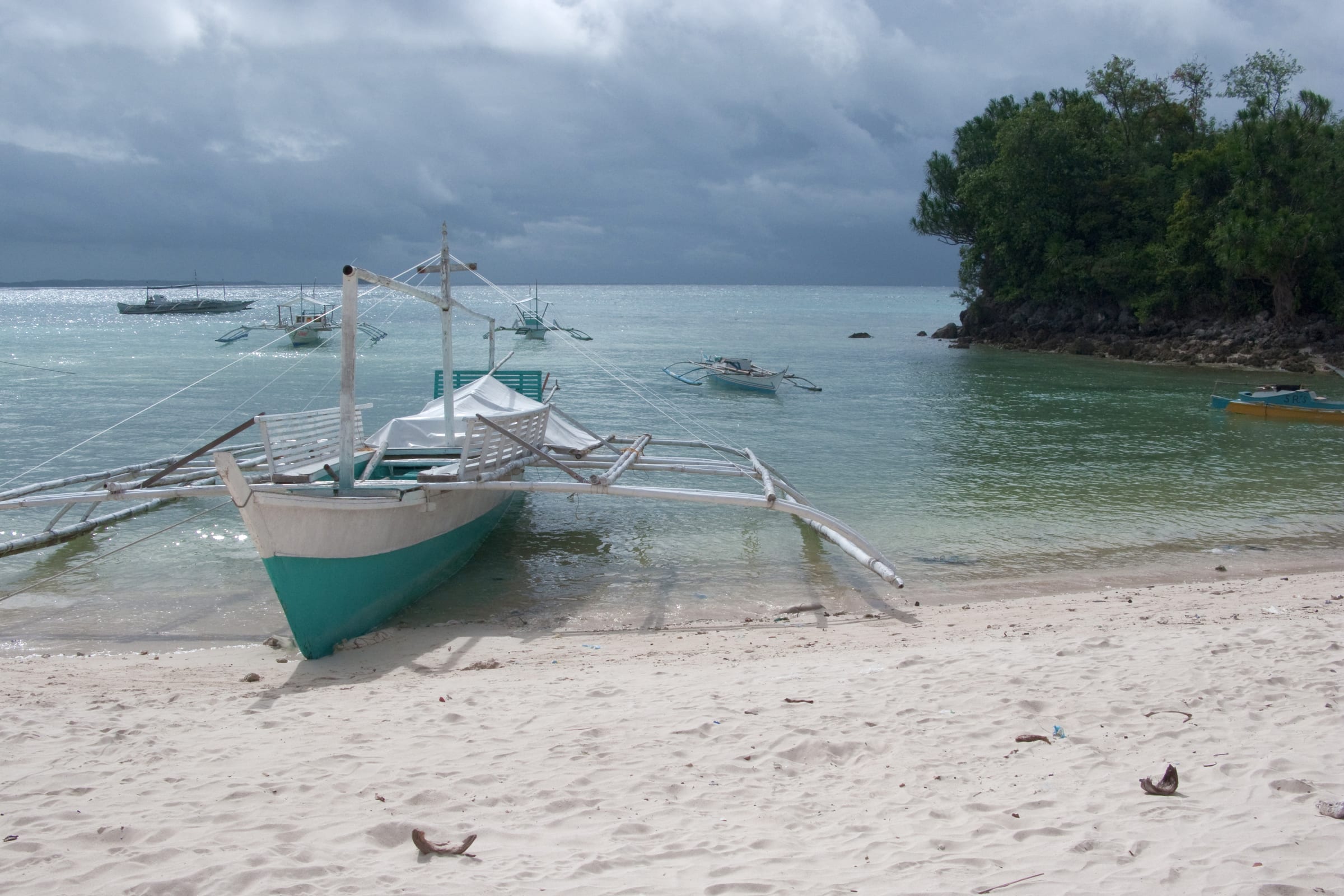 Traditional outrigger boat on a pale sandy beach beside turquoise water