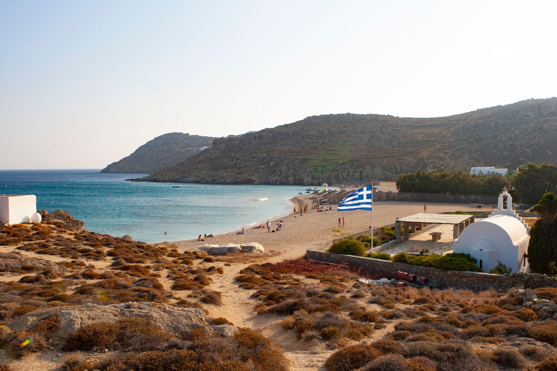 Sandy bay with turquoise shallows, dry hills and a whitewashed chapel