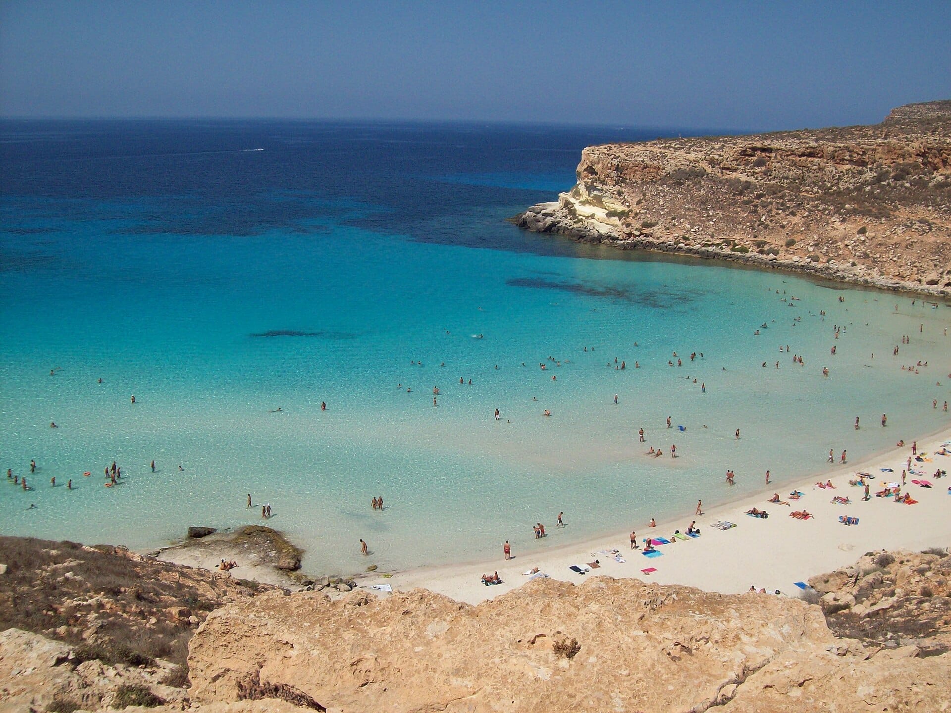 Swimmers in the pale turquoise bay of Spiaggia dei Conigli, Lampedusa, seen from the low cliffs