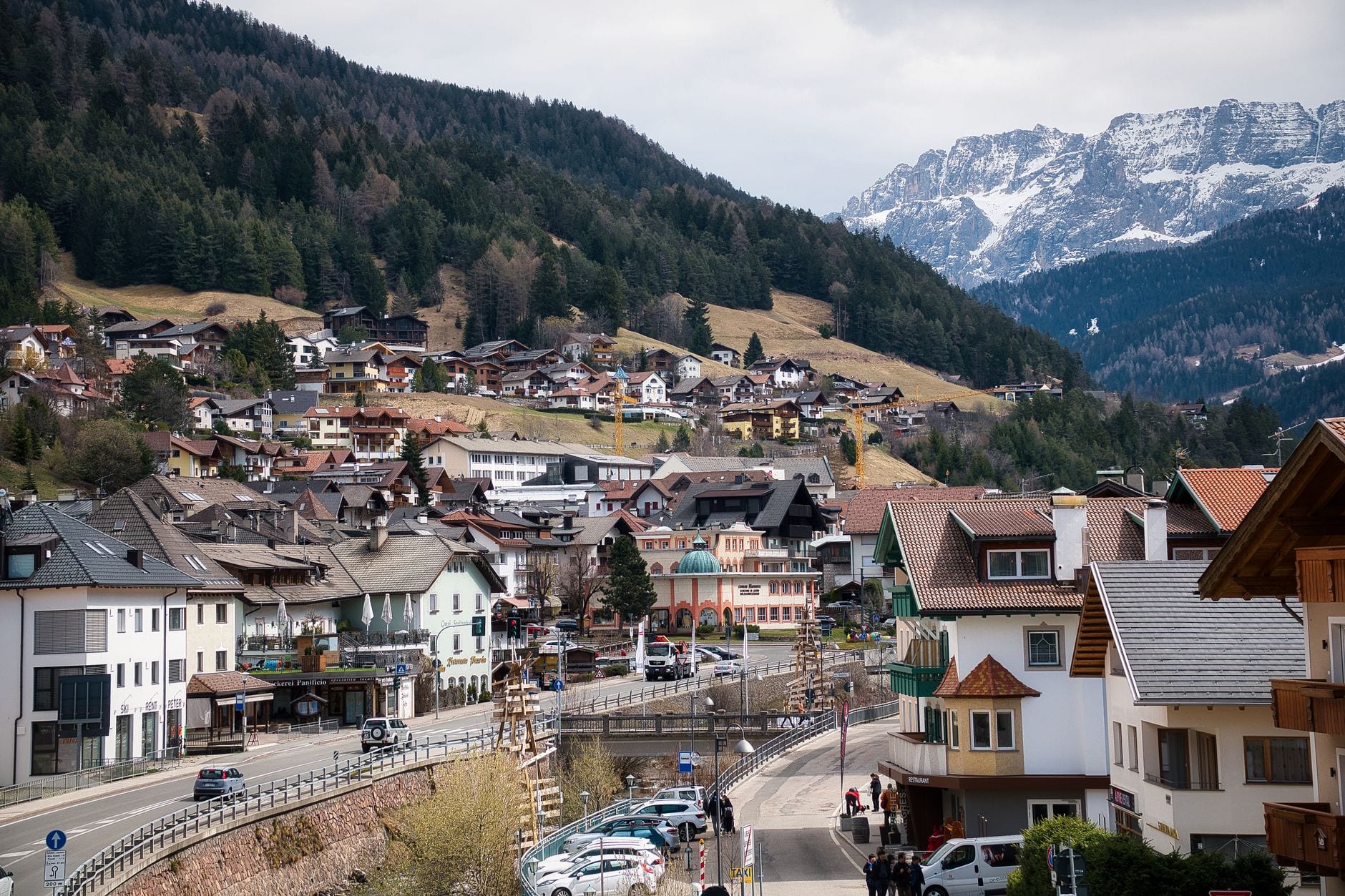 Hotels and chalets stacked above the valley road in Ortisei, Val Gardena, with snow still lying on the Dolomite peaks behind