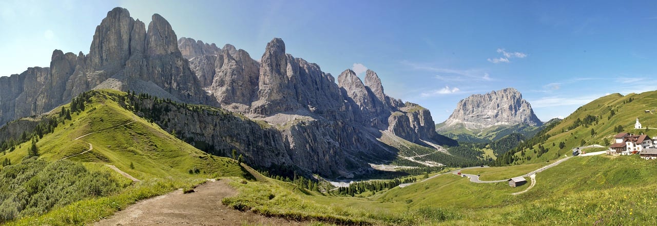 Green pasture and a hairpin road below jagged limestone peaks at the Passo Gardena, with the Sassolungo group in the distance