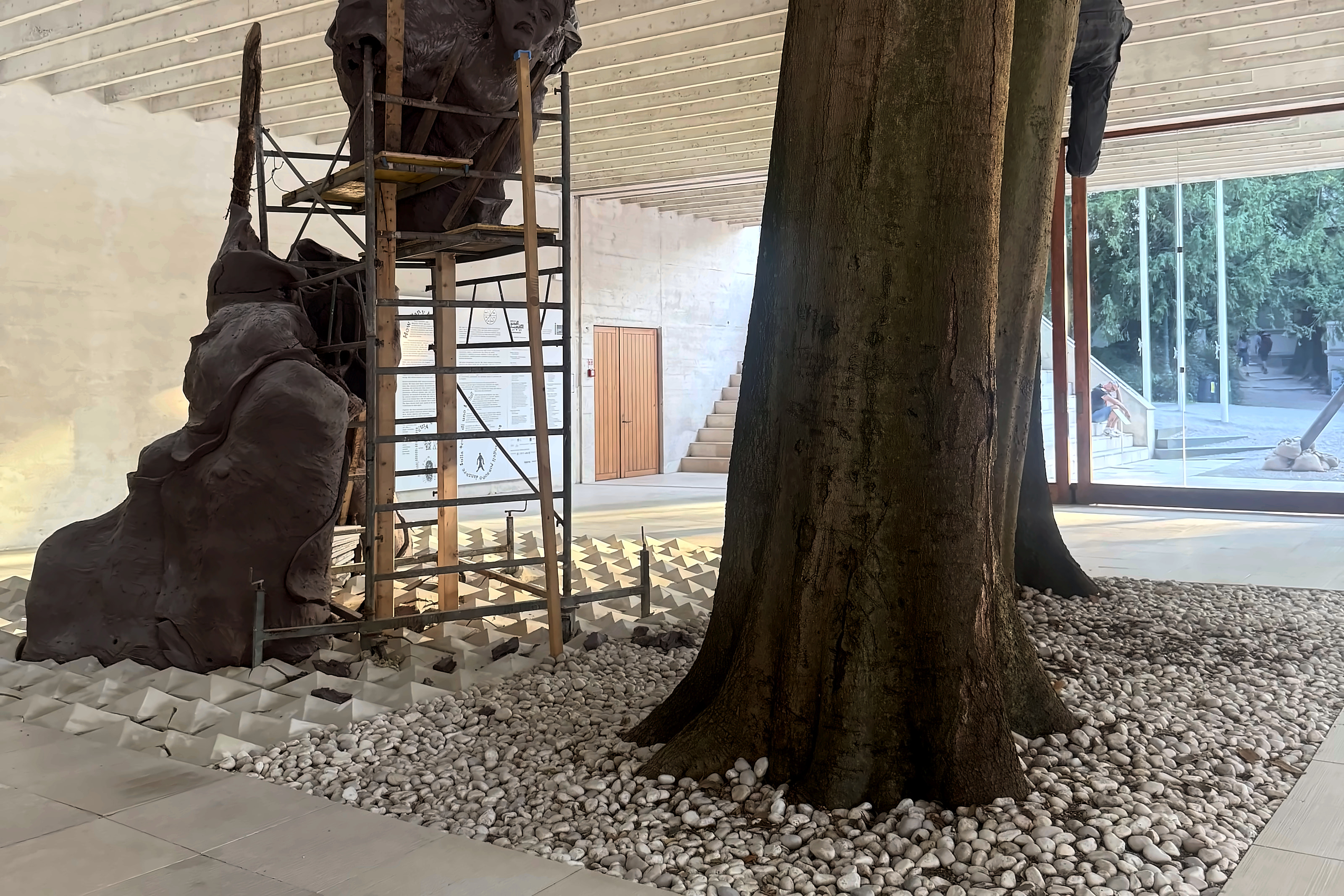 A living tree rising through a pavilion beside a sculpture on scaffolding