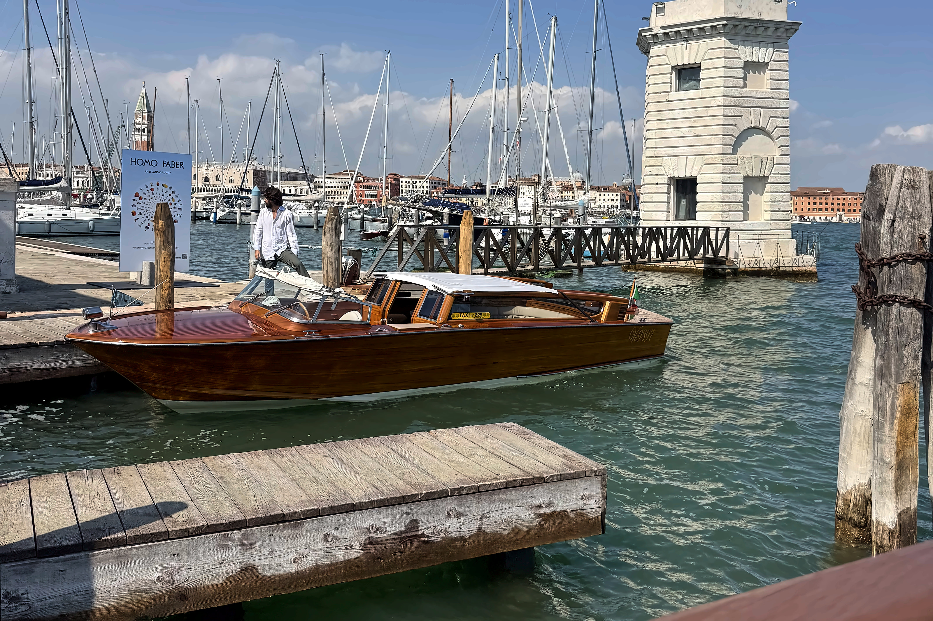 A varnished wooden launch moored beside the white lighthouse of San Giorgio Maggiore