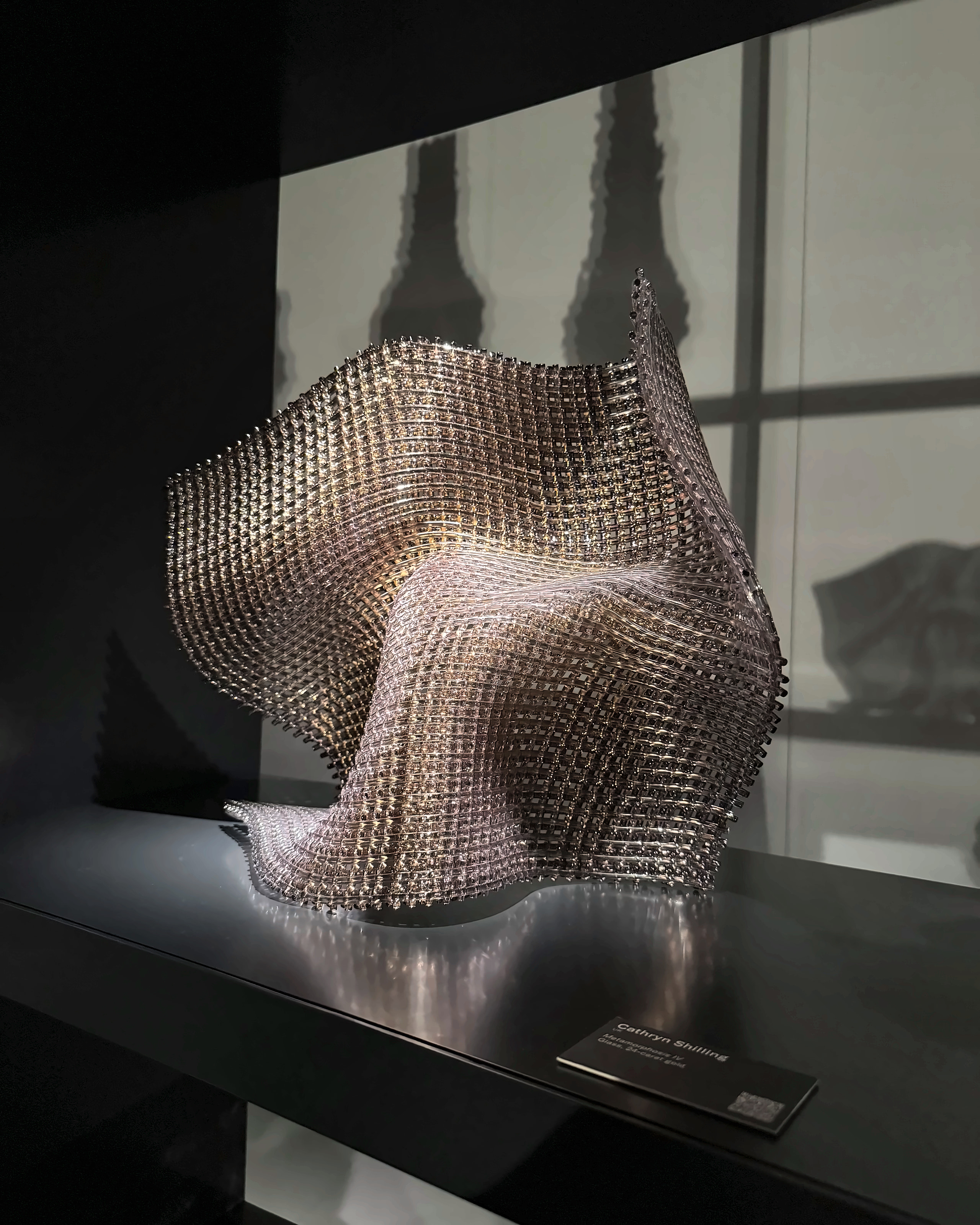 A rippling sculpture of woven metal lit against a dark wall