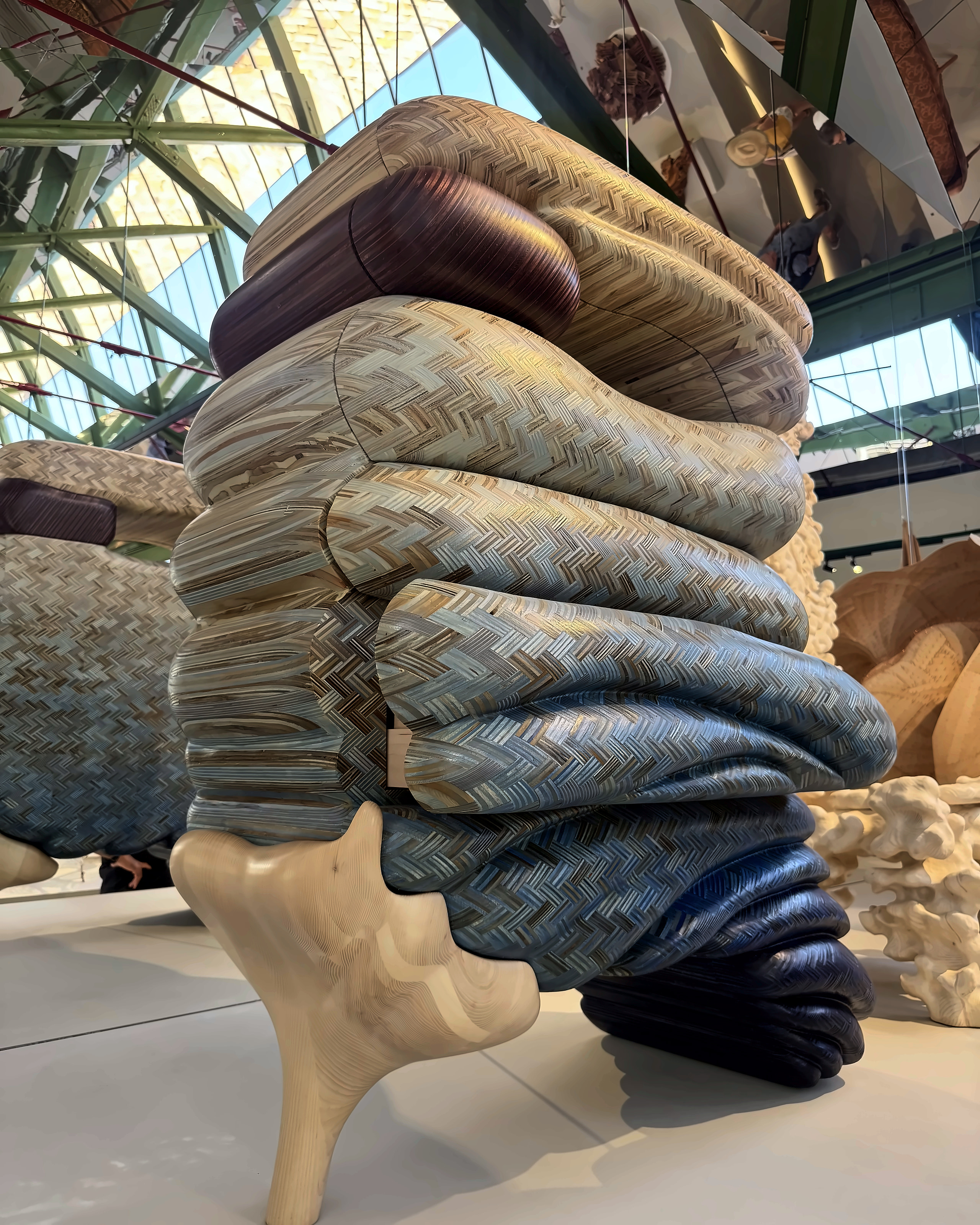 A tall stack of woven textile forms on carved wooden legs